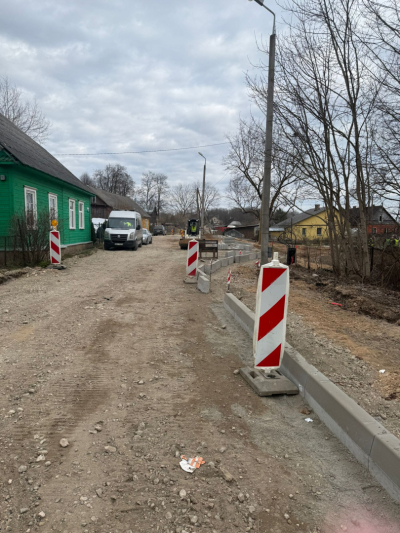 Atsākti ielas pārbūves darbi Strādnieku šķērsielā Ludzā: uz sabērtas šķembu pamatnes tiek uzstādītas jaunas betona apmales un redzami sarkani balti brīdinājuma signālstabiņi.